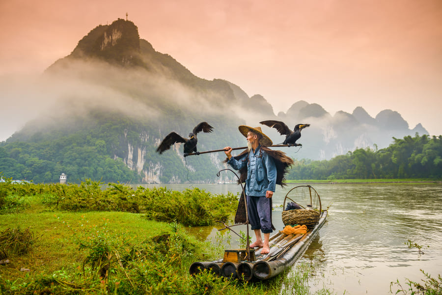 pescador con cormoran sobre una lancha en el rio Yulong en Yangshuo con montañas de fondo